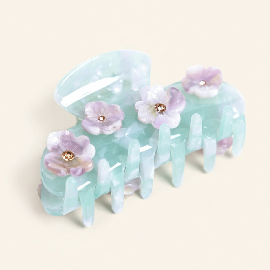 Set of three light blue hair clips with floral designs on a beige background